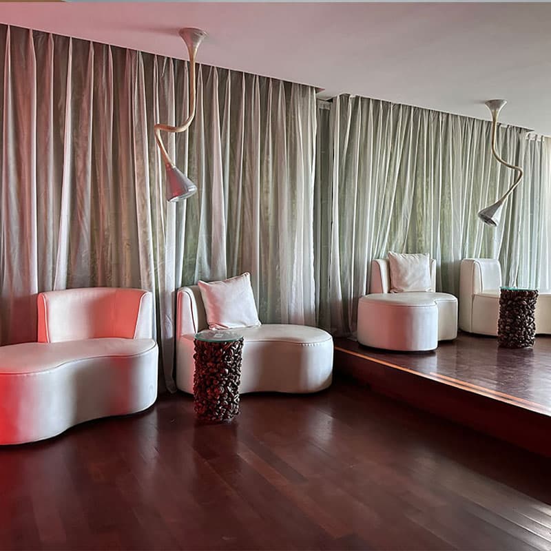 A stylish lounge space featuring organic-shaped white seating on dark hardwood floors with sheer curtains and artistic sculptural floor lamps.