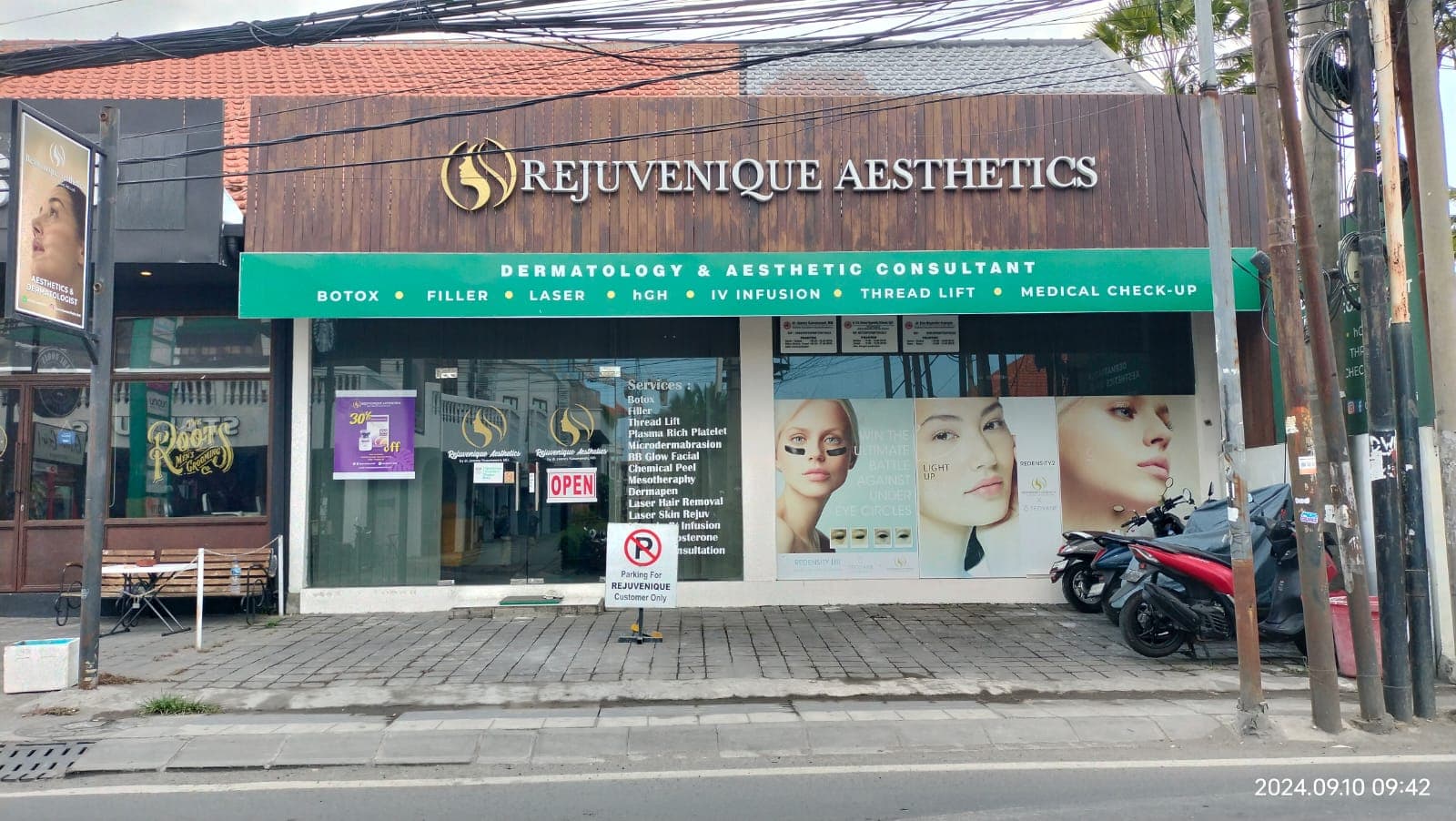 Street-level exterior view of Rejuvenique Aesthetics clinic storefront showing signage, promotional posters, and parked motorcycles on a Bali street.