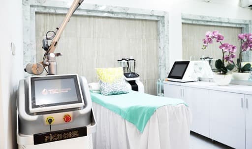 Clean treatment room featuring a Pico One laser device, treatment bed with teal covering, and orchid accents, though the composition is slightly cluttered with multiple equipment pieces.