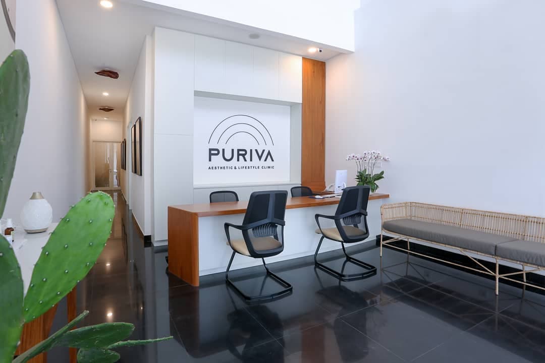 Wider-angle view of the sleek reception area featuring the branded wall, rattan waiting bench, polished dark floors, and lush greenery framing the modern minimalist space.