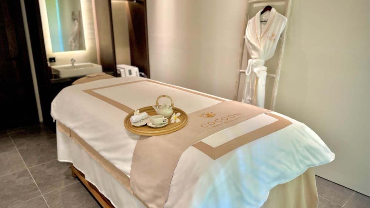 Elegant spa treatment room featuring a branded massage bed with tea service, white robe, and backlit mirror, conveying a premium wellness experience.