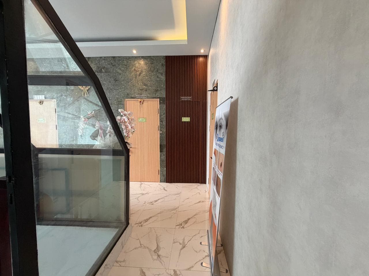 Narrow hallway corridor with marble flooring, wooden slatted accent wall, recessed lighting, glass partition, and orchid decoration.