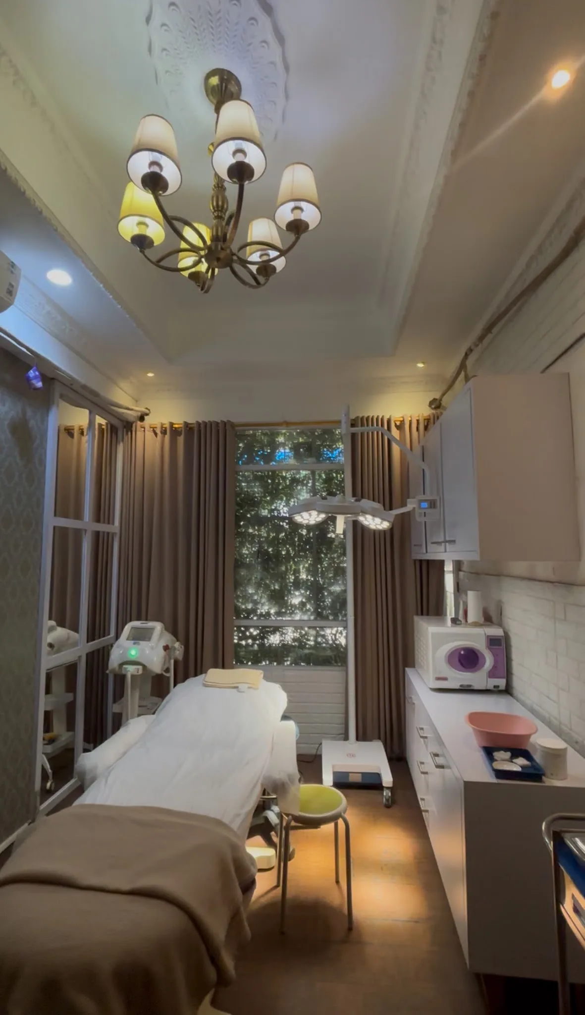 Clinic entrance and lobby area at night showing glass doors with reversed DNI Skin Centre logo, patterned wallpaper with illuminated display niches, mostly empty shelves, and a maroon sofa edge. Closed sign visible, empty and somewhat sterile feel.