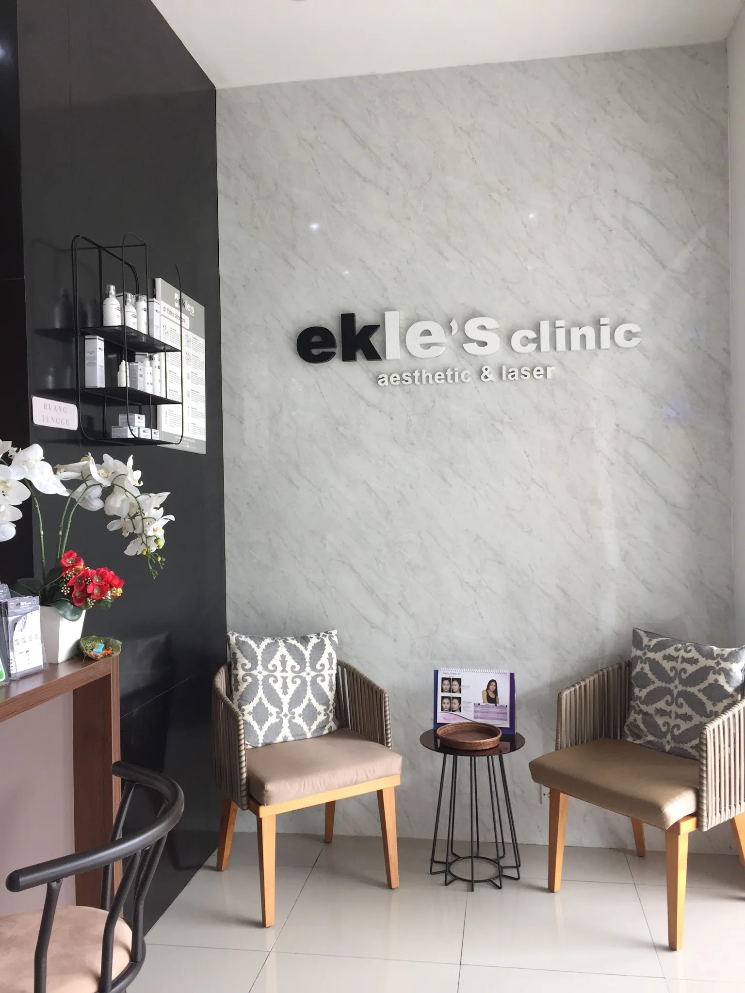 Clinic lobby with curved velvet bench, gold-framed product display, sputnik chandelier, marble flooring. Promotional banner detracts.