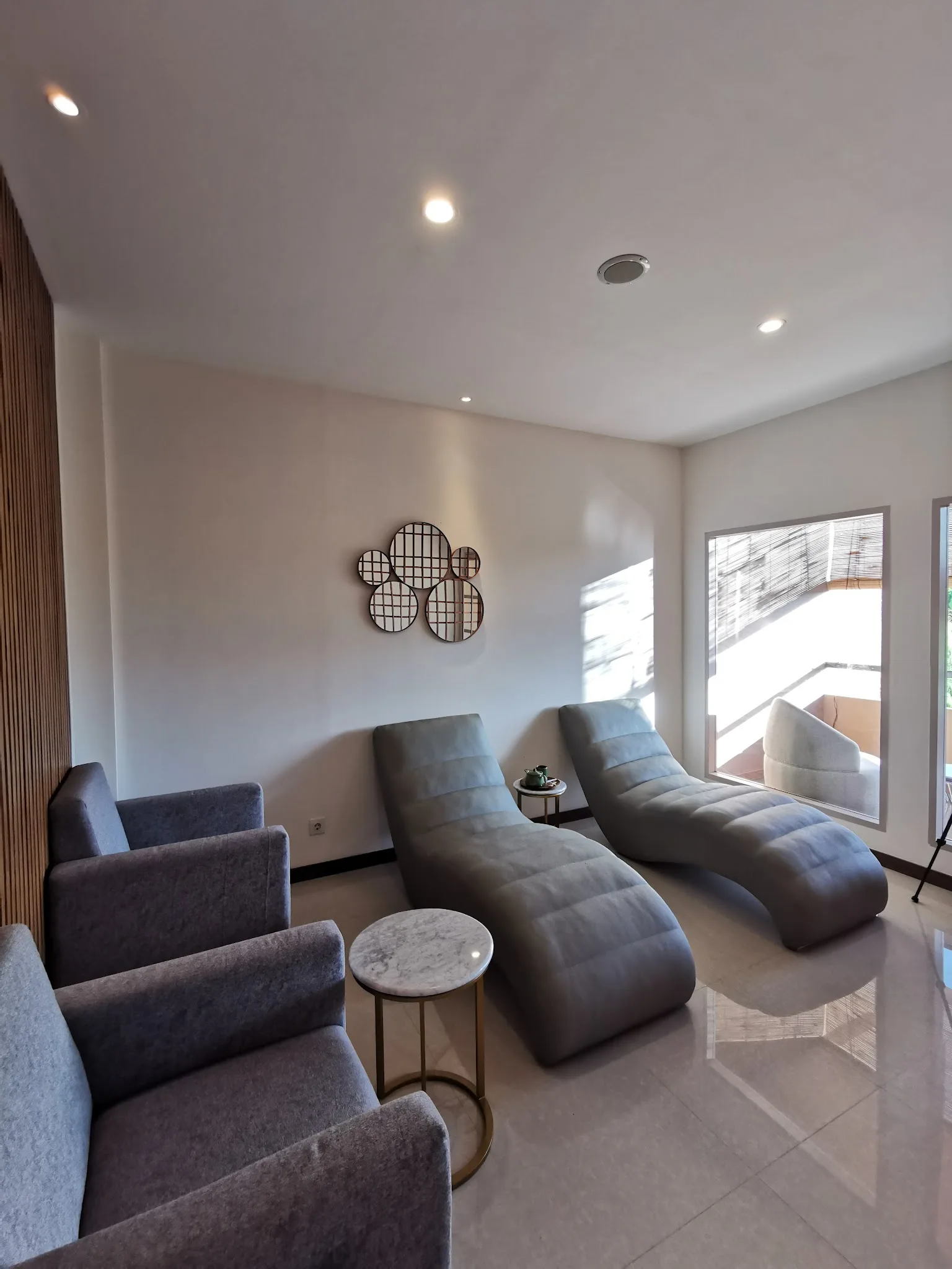 Waiting area with two grey lounge chairs, a small wooden side table, and a wall-mounted product display shelf; visible ceiling stains and worn walls reduce the premium aesthetic quality significantly
