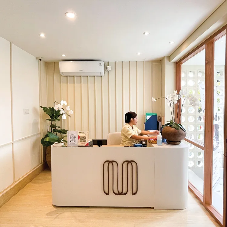 Clean treatment room with a neatly prepared branded bed, professional skincare equipment, ambient curved wall lighting, and warm curtain backdrop conveying a professional service environment.