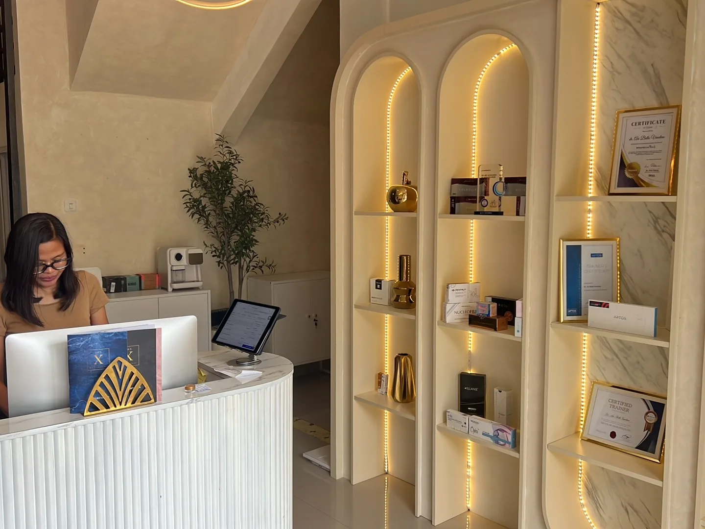 Chic waiting area with a plush cream armchair, marble coffee table with magazines, Dermalogica branded display shelf, framed artwork.