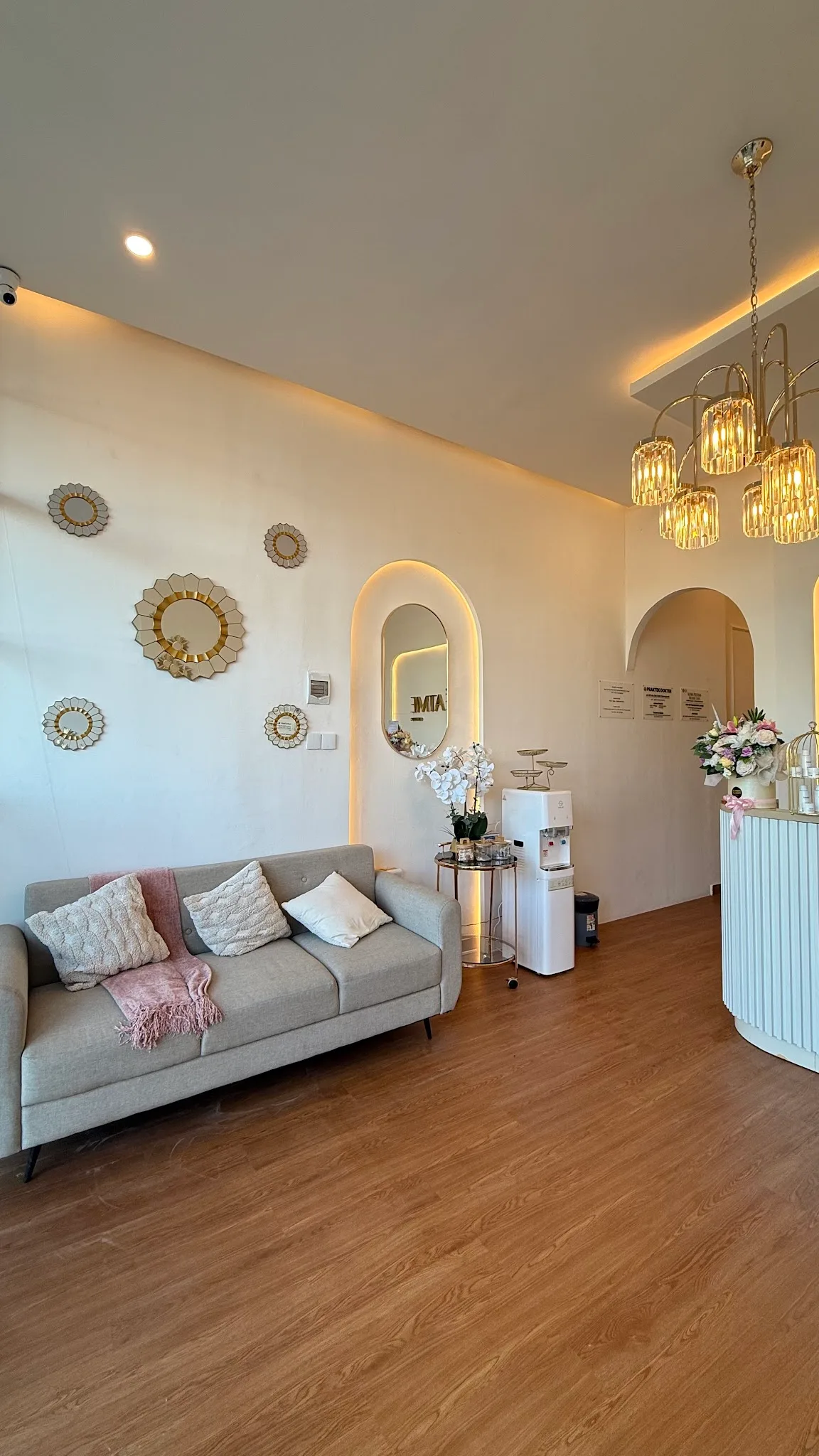A cleaner straight-on view of the clinic hallway with elegant wainscoting, sunburst mirrors, and arched architecture, though the visible fire extinguisher and dim warm lighting slightly lower the premium feel.