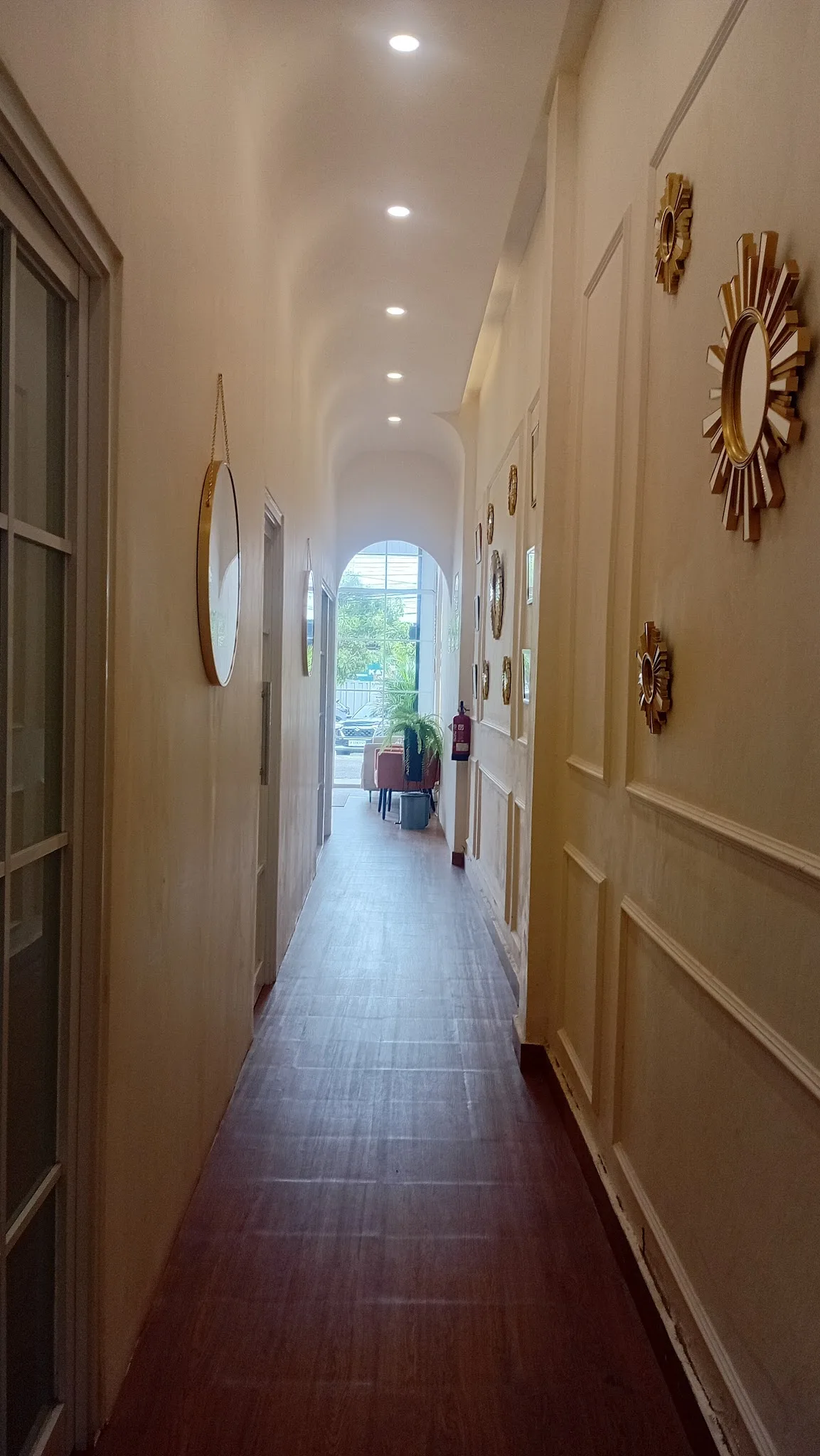 Hallway with wainscoting, decorative gold mirrors, and an arched opening leading to natural light, though the slightly tilted angle and dim lighting reduce the overall quality.